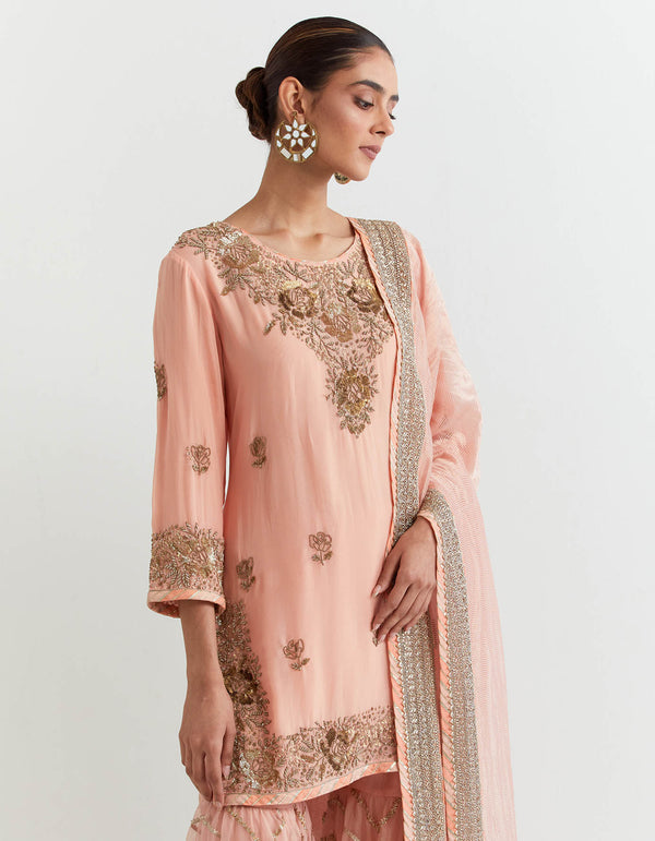 Peachy pink organza silk kurti in hand embroidery paired with chevron gota embroidered sharara and dupatta